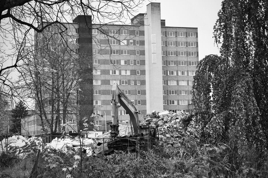A construction excavator amidst rubble in front of a high-rise building.