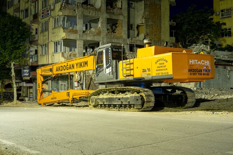 Large excavator at a demolition site at night under lights.